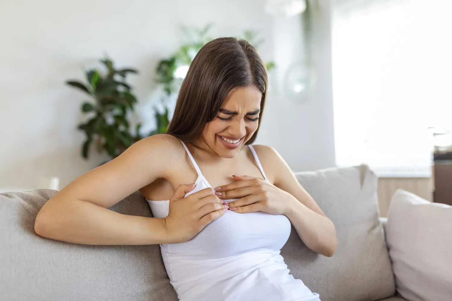Woman sitting with strong chest pain and hands touching her chest while having trouble at home, heart attack or heart failure symptom